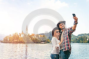 Happy couple of tourists in love take a selfie on a smartphone on the background with Bled Lake and Church on the Island, Slovenia