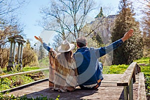 Happy couple of tourists relaxing by Olesko Castle in spring park raising arms. Travelling in Western Ukraine