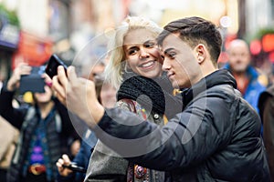 Happy couple of tourists taking selfie in a crowded street.