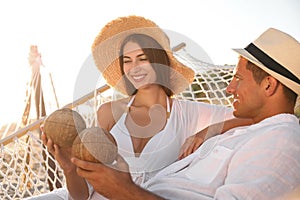 Happy couple with tropical cocktails relaxing in hammock on beach