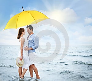 Happy couple with umbrella for sun protection on beach near sea