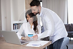 Happy couple using bank card and laptop while shopping onlie