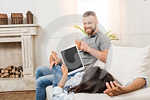 Happy couple using digital tablet while lying on sofa at home