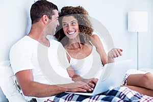 Happy couple using laptop on bed