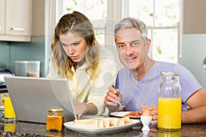 Happy couple using laptop and having breakfast