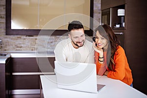 Happy couple using laptop in the kitchen at home