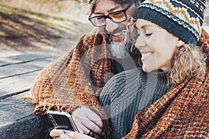 Happy couple using phone device together in outdoor leisure activity and romantic day at the park. Love and relationship sharing