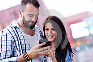 Happy couple using smartphone in city in rainy day