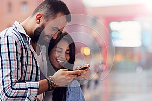 Happy couple using smartphone in city in rainy day