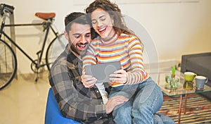 Happy couple using tablet for home wifi system - Young people having fun with tech online household device - Technology trends,