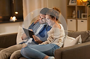 Happy couple using tablet pc at home in evening