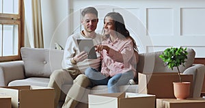 Happy couple using tablet talking on sofa on moving day