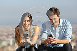 Happy couple using their smart phones outside