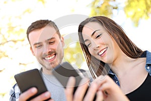 Happy couple using their smart phones in a park