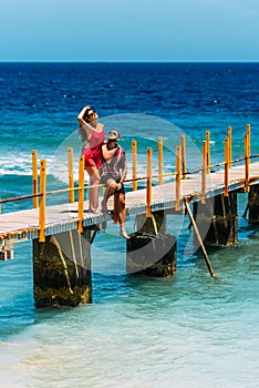 Happy couple on vacation strolling along a wooden pier above the tropical turquoise ocean.