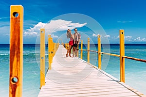 A happy couple on vacation strolling along a wooden pier above the tropical, turquoise ocean in Bali, Indonesia.