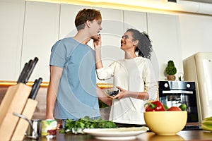 Happy couple, vegetarians preparing healthy meal, sandwhich, salad in the kitchen together. Girl feeding her boyfriend