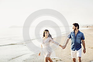 Happy couple walking along the sea, holding hands. The girl has a flower wreath on her head. Love story