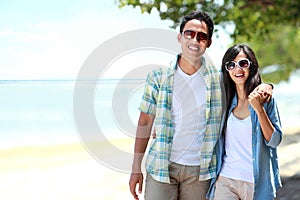 Happy couple walking by the beach together in love holding around each other