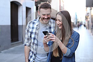 Happy couple walking using cell phone in the street