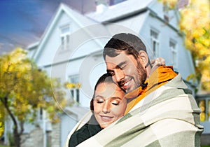 happy couple in warm blanket over house in autumn