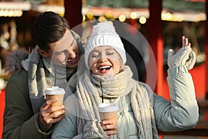 Happy couple in warm clothes with drinks at winter fair