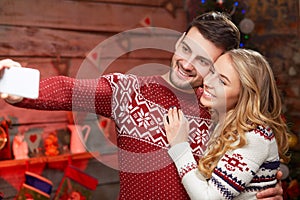 Happy couple in warm sweaters taking selfie picture in christmas