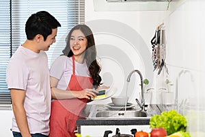 Happy couple washing dishes together in the sink in the kitchen at home