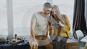 Happy smiling couple watching photos from travel on digital camera at home after vacation