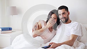 Happy couple watching tv in bed at home