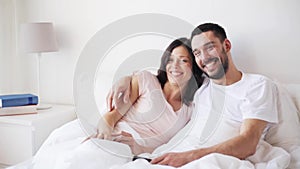 Happy couple watching tv in bed at home