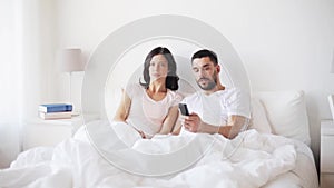 Happy couple watching tv in bed at home