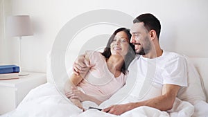 Happy couple watching tv in bed at home