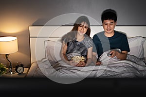 Happy couple watching TV on a bed at night