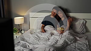 Happy couple watching TV on a bed at night