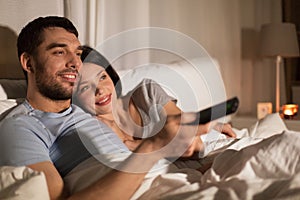 Happy couple watching tv in bed at night at home