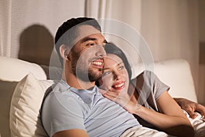 Happy couple watching tv in bed at night at home