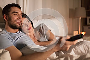 Happy couple watching tv in bed at night at home