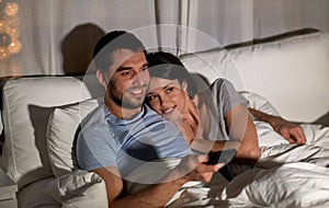 Happy couple watching tv in bed at night at home