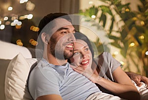 Happy couple watching tv in bed at night at home