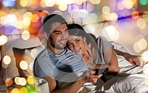 Happy couple watching tv in bed at night at home