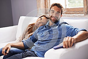Happy couple, watching tv on sofa and relax together in living room with streaming service, trust and hug for bonding