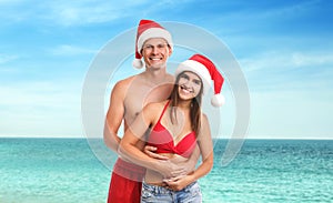 Happy couple wearing Santa hats near sea. Christmas vacation