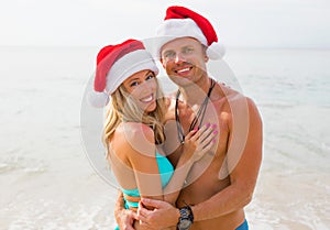 Happy couple wearing Santa hats on the beach