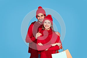 Happy Couple Wearing Winter Clothes Embracing And Holding Shopping Bags