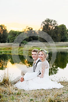 Happy couple in wedding attire on lake background at sunset, the bride and groom in a white dress.