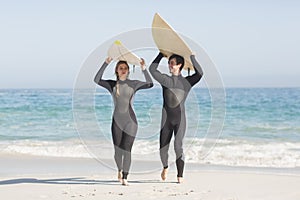 Happy couple in wetsuit carrying surfboard over the head