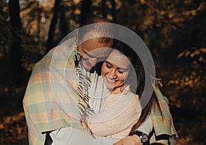Happy couple of wife and her husband shelter in plaid in the fall. Close up holding hands. Cheerful family are smiling.