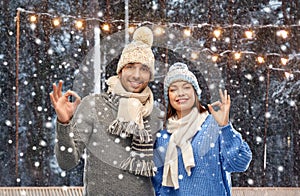 happy couple in winter clothes showing ok sign