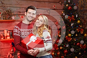 Happy Couple in winter pullovers smiling and holding big red gift box